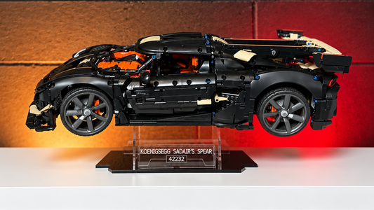A black LEGO Koenigsegg car on a clear display stand, set on a white shelf against a dark brick wall with warm and red lighting.
